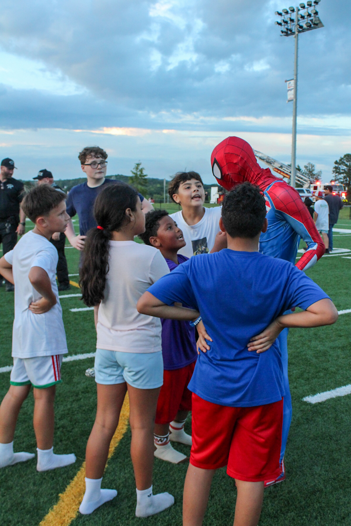 Spider-Man surrounded by children on a sports field